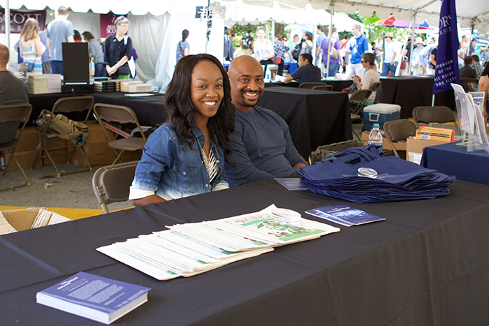 Two people sit at the Emory tent, ready to offer free totes and information to festival participants.