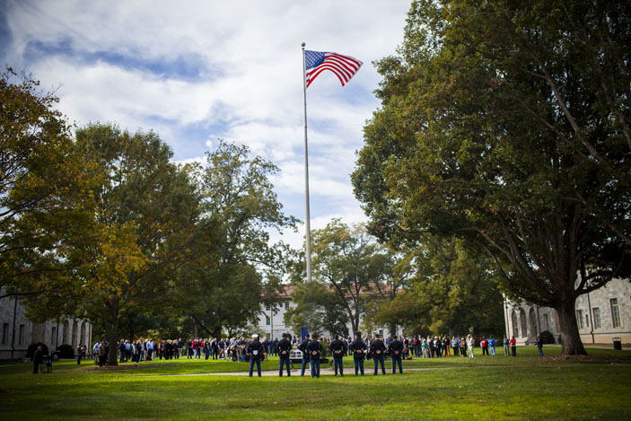 the U.S. flag flies on the Emory Quad. A color guard surrounds the base of the flagpole with the audience in the background.