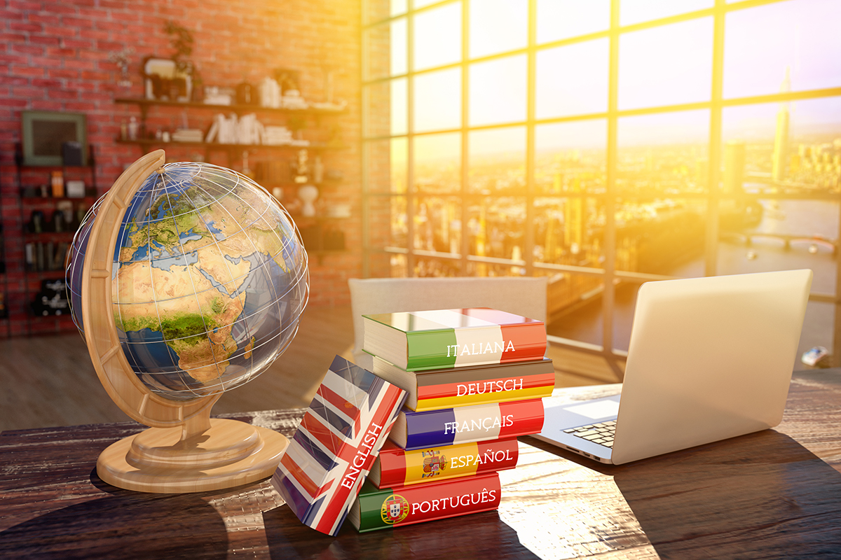 Stock image of a globe, a stack of books, and a laptop in a sunny interior room