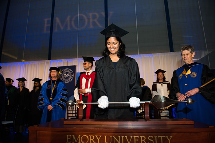 An Emory graduate holds a baton. 