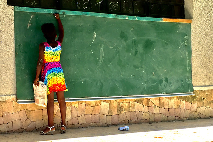 A young girl from Haiti writes on a large, outdoor chalkboard.