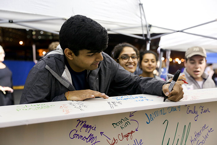 A student adds his name to the top of the beam in black marker.