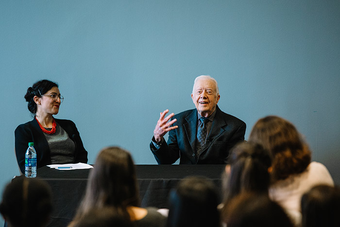 President Jimmy Carter smiles and talks with his hands to a class of eager students.