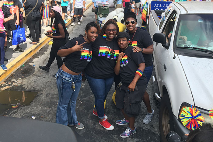 A group of four stand stop in the street to pose for a photo while marching in the Atlanta Pride Parade, representing Emory University.