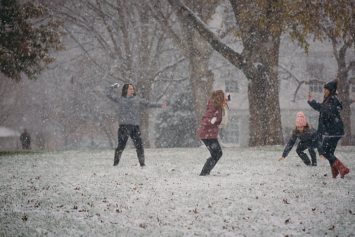 Four students are all smiles as they throw snowballs at each other.