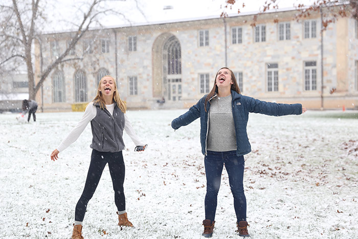 Two female students try to catch snowflakes on their tongues.