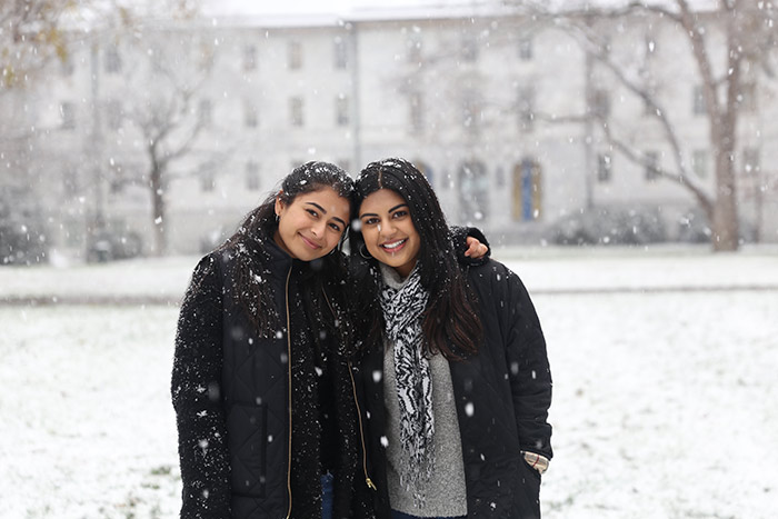 Two students pose for the camera while snow falls all around them.