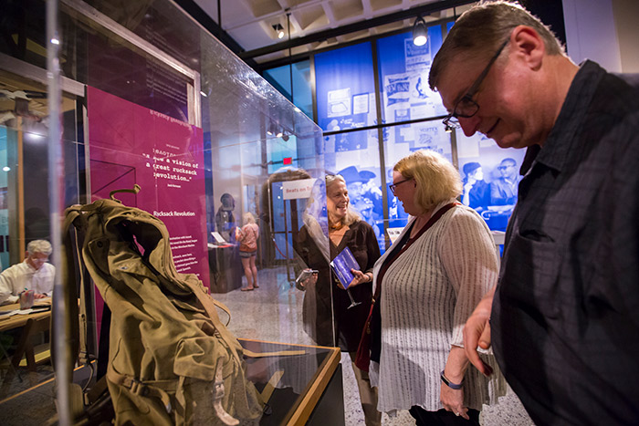 Attendees stand in front of a glass case to view Jack Kerouac's rucksack.