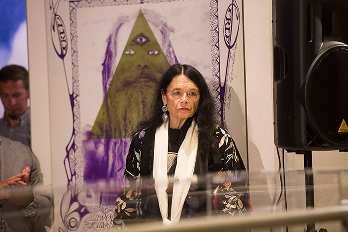 Anne Waldman stands in front of a display at the exhibit opening.