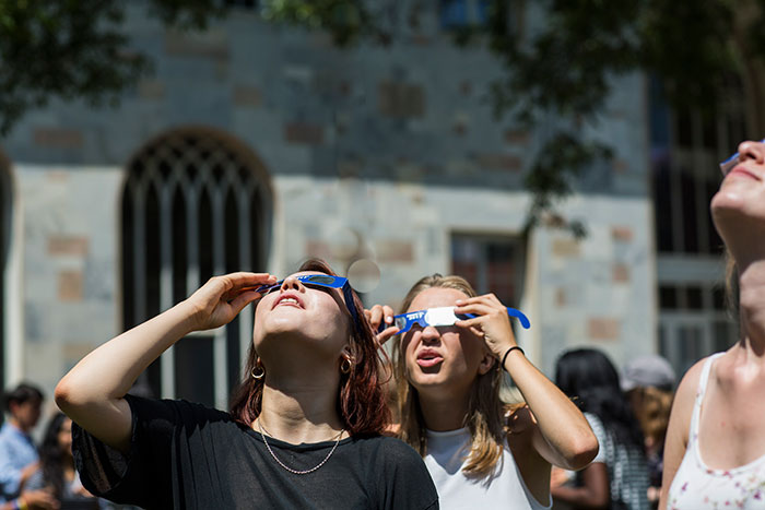 Students look through special glasses at the eclipse above.