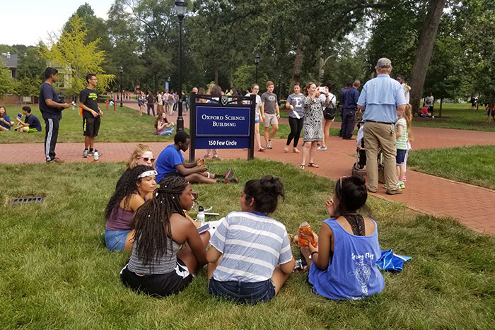 Students sit in the grass to watch the eclipse overhead.