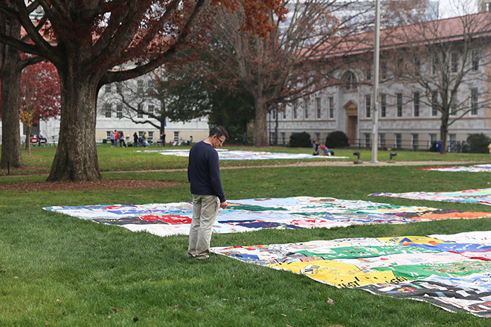 An adult male stands in front of a quilt, reading the names.
