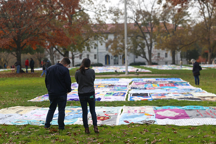 Two students stand in front of a quilt, reading the names.