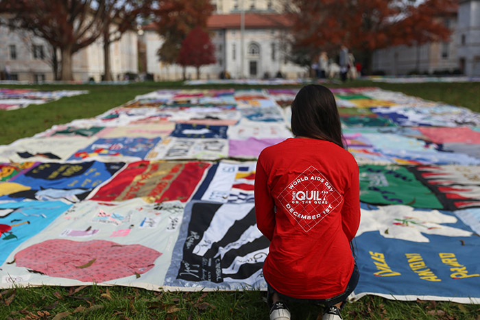 A young woman wearing a t-shirt from the event, kneels in front of a quilt.