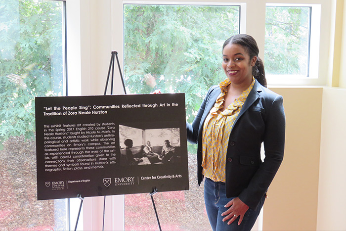 Professor Nicole Morris stands next to a sign at the opening of her class's exhibit.