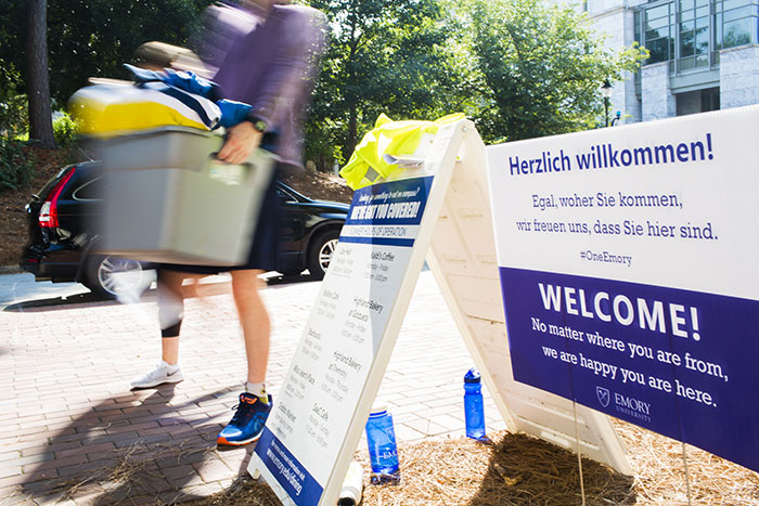 Students walk past welcome signs, carrying bins