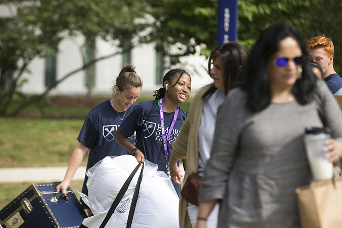 Student volunteers help students move in by rolling their belongs into the dorms