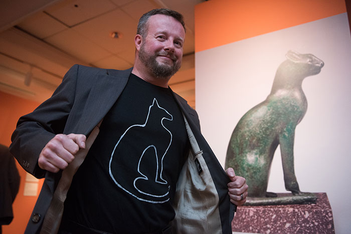 A museum attendee dons a cat t-shirt while posing with a cat sculpture on display