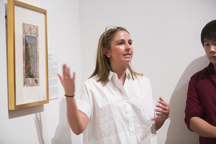 A young woman speaks to a crowd about a particular work of art on display
