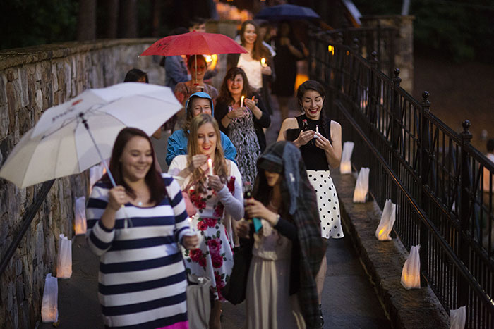 A large group of students walk across the bridge over Houston Mill Road carrying umbrellas and candles for the Candlelight Crossover