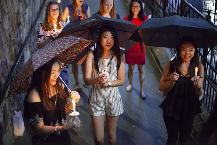 A group of students walk across the bridge with umbrellas