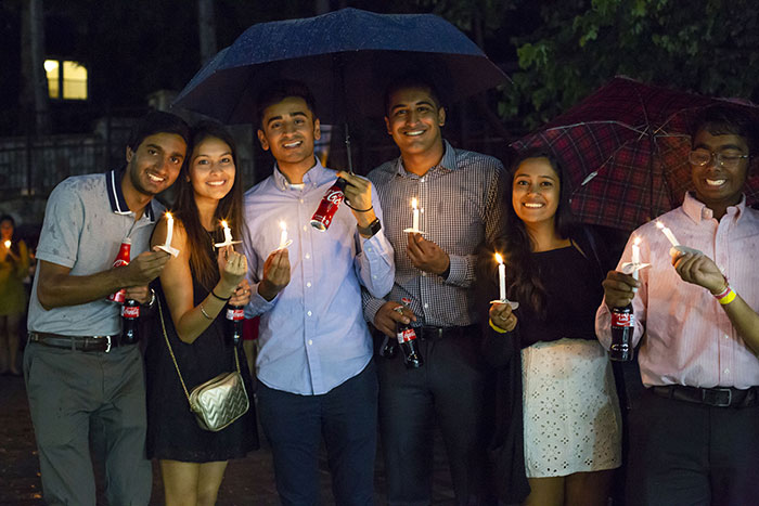 A group of students pose under shared umbrellas with their candles and Cokes