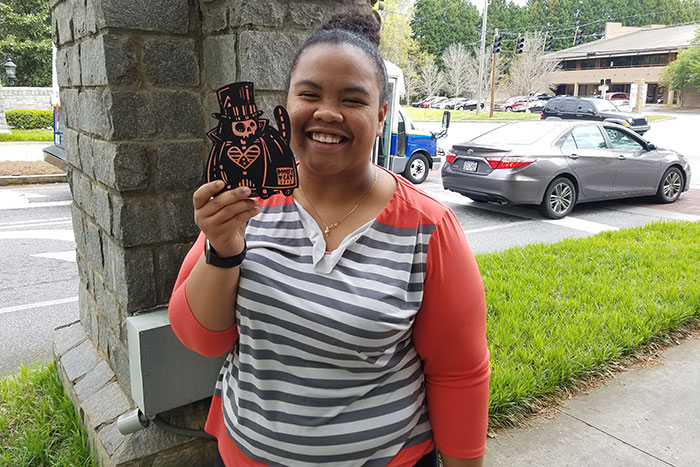 A student poses with a wooden, black and orange "Dooley Cat" she found on Emory's campus