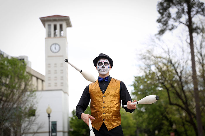 A performer with a painted skeleton face mask juggles three pins