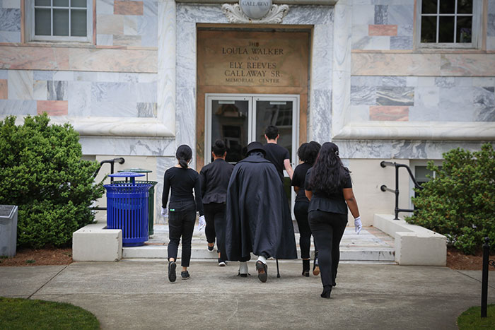 Dooley walks through campus with groupies all dressed in black clothing and sunglasses