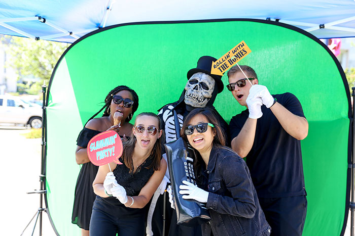 Four Emory students and Dooley pose with props in front of a green screen in a photobooth for Dooley's Week