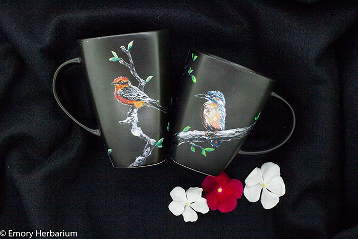Two black mugs of different sizes handpainted with colorful plant designs