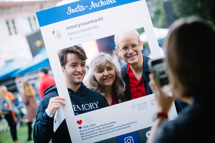 A family poses for a selfie with a cardboard frame for Emory Homecoming