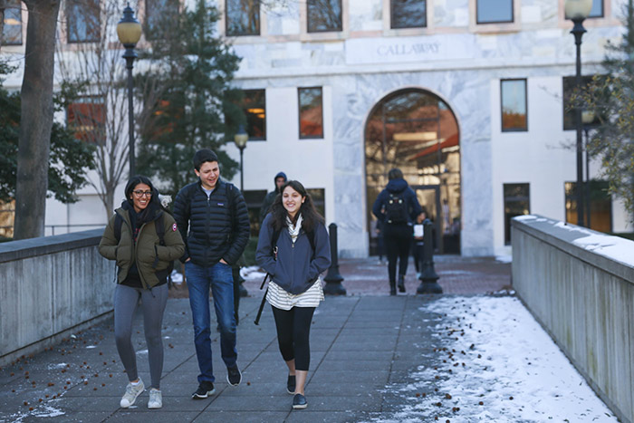 Three students walk across a bridge on campus
