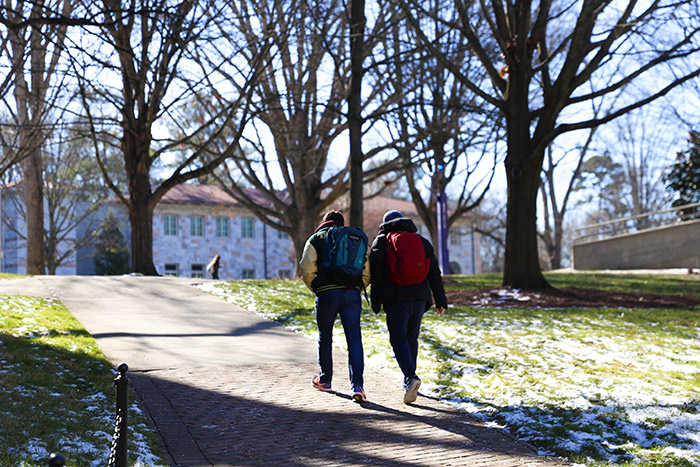 Two students wearing backpacks walk across campus