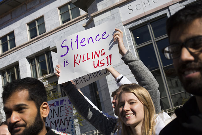 A male student holds up a sign that reads: "Silence is killing us"