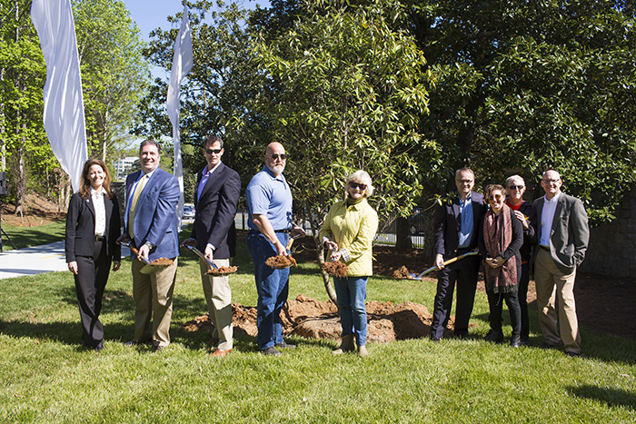 The same seven representatives pose with shovels as they plant a magnolia tree.