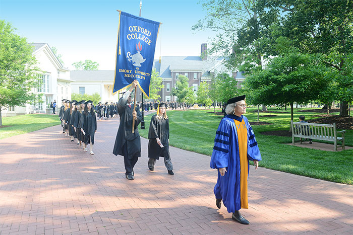 An Emory leader leads a procession of students. A student holds the Oxford College banner.