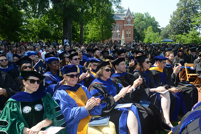 Emory faculty, many wearing sunglasses, applaud from their seats