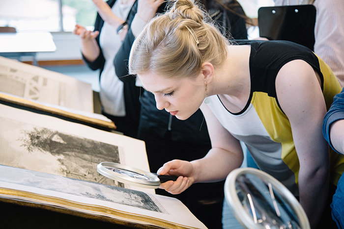 A student uses a magnifying glass to examine the details on a Piranesi etching.