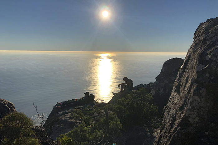 A student sits on a rock, viewing a sunset from atop Cape Town's Table Mountain