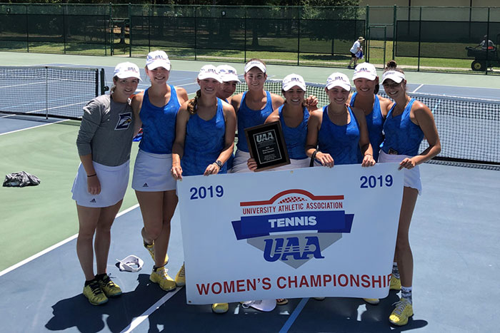 The Emory women's tennis team poses with a banner naming them UAA champions