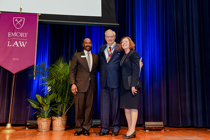 Richard Hubert stands between Dean Hughes and Emory President Claire E. Sterk on a stage.