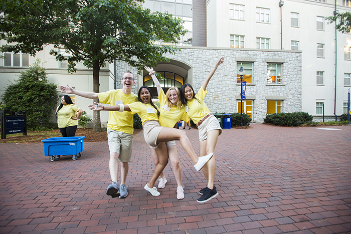 Resident Assistants in matching yellow t-shirts excitedly welcome new students moving in
