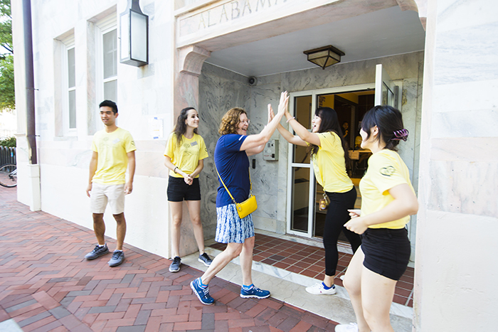 Resident Assistants in matching yellow t-shirts excitedly welcome new students moving in and give a high five to Emory President Claire E. Sterk