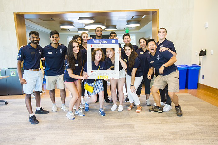 Resident Assistants in blue pose for a photo with Emory President Claire E. Sterk