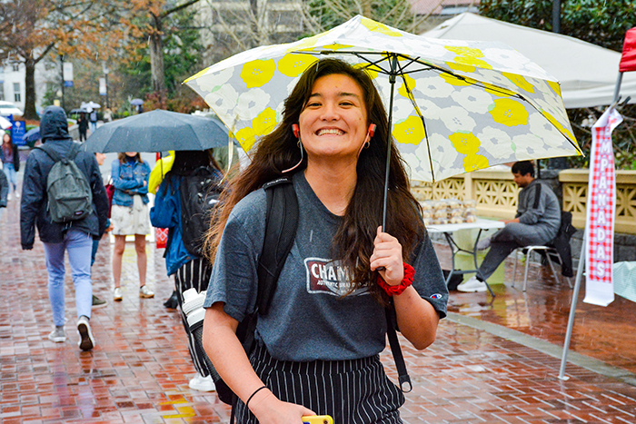 A student carries an umbrella and smiles as she walks through Asbury Circle in the rain