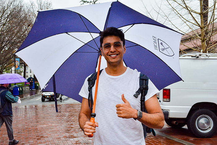 A student carries an umbrella and smiles as he walks through Asbury Circle in the rain