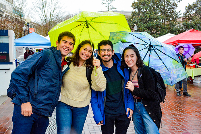 Four students stand under an umbrella in Asbury Circle