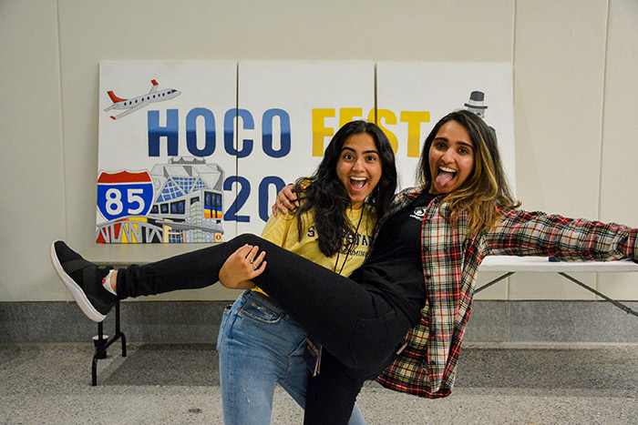 Two students pose in front of a HoCo 2019 poster