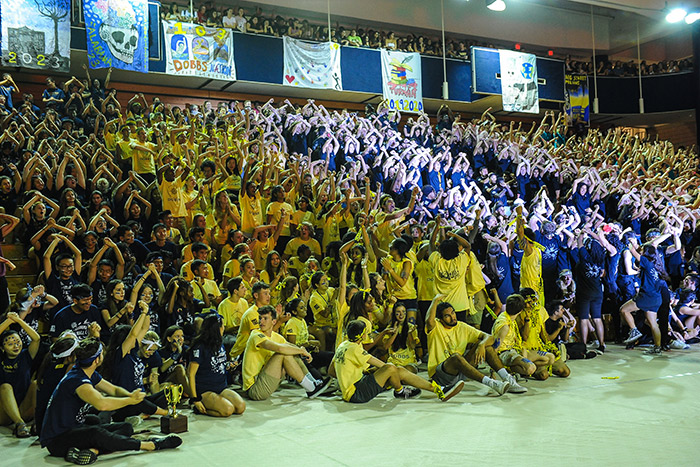 A large crowd of students in multi-colored t-shirts cheer at Songfest